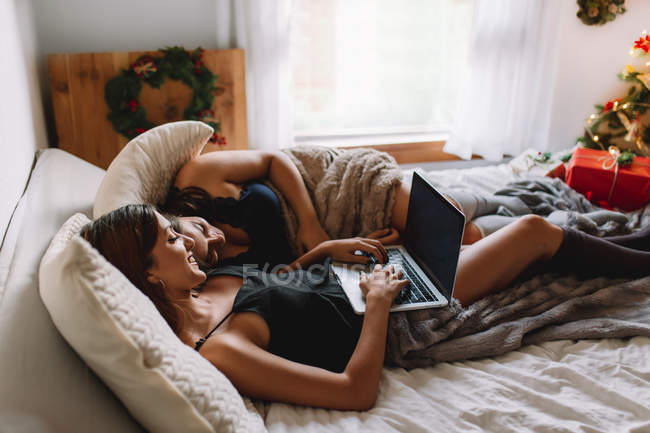 Due amiche che utilizzano il computer portatile a letto in accoglienti interni di Natale
. — Foto stock
