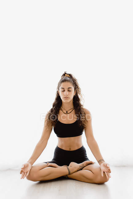 Tranquilla donna di razza mista in abbigliamento sportivo meditando su sfondo bianco — Foto stock