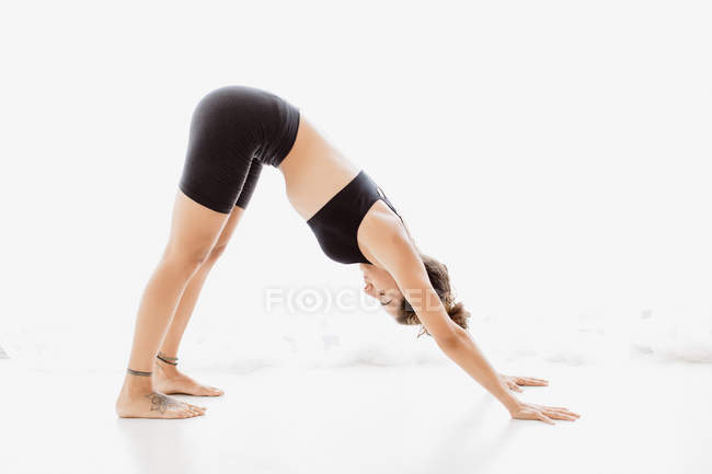 Fit  woman performing downward-faced dog yoga pose in studio — Stock Photo