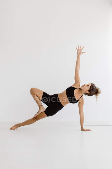 Mujer deportiva que realiza postura de yoga de tablón lateral sobre fondo blanco - foto de stock