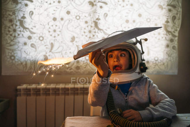 Fantasizing boy in astronaut helmet playing with paper plane at home — Stock Photo