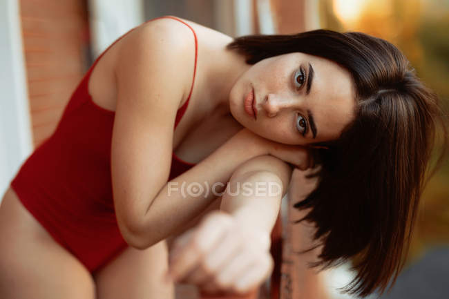 Jovem mulher séria com cabelo escuro em bodysuit brilhante inclinando-se sobre trilhos e olhando para a câmera em fundo borrado — Fotografia de Stock