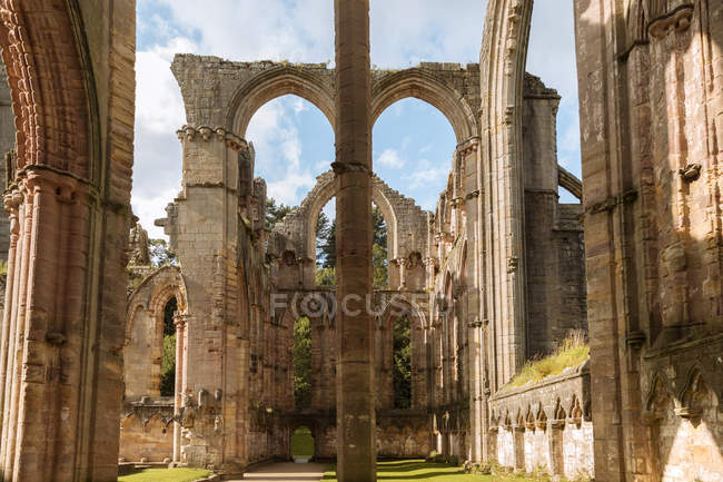 Historical stone building with arched passages and green grass on cloudy sky background in Abadia de Fountains — Stock Photo