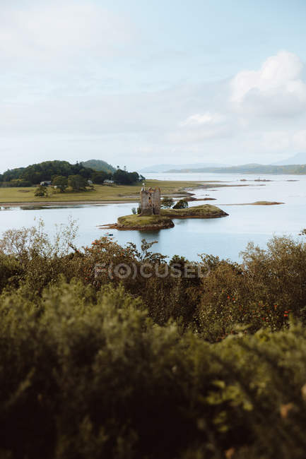 Danneggiato vecchio castello situato sulla costa del lago calmo contro colline erbose il giorno nuvoloso nella campagna britannica — Foto stock