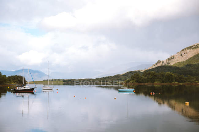Paisaje pintoresco de montaña y cielo nublado reflejado en aguas tranquilas con veleros en Glencoe durante el día. - foto de stock