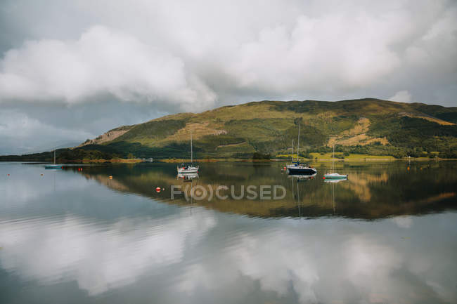Paisagem pitoresca de montanha e céu nublado refletida em águas tranquilas com veleiros em Glencoe durante o dia — Fotografia de Stock