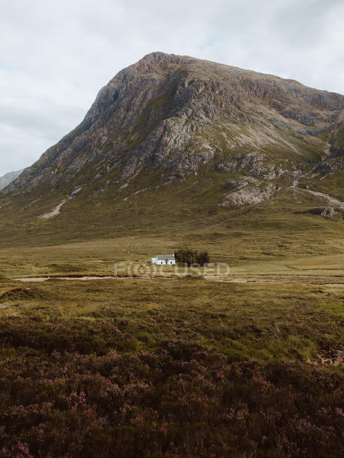 Picturesque view of white building and trees in middle of green valley by high rocks in Glencoe on daytime — Stock Photo
