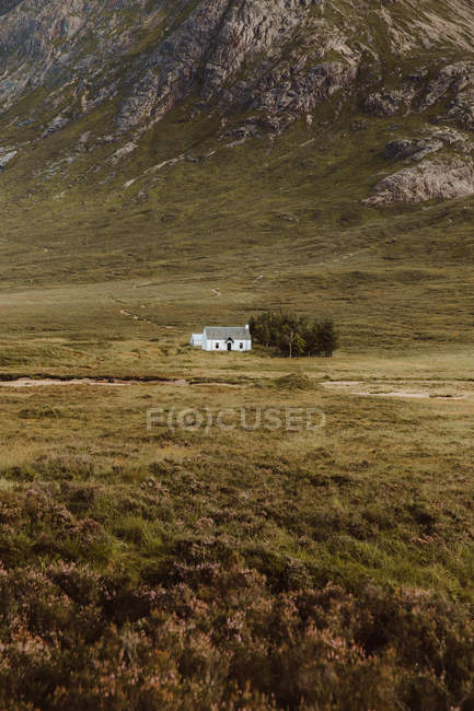 Picturesque view of white building and trees in middle of green valley by high rocks in Glencoe on daytime — Stock Photo