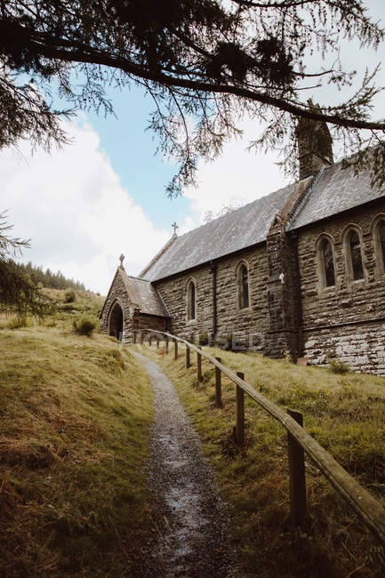 De abaixo da estrada com grade de madeira que conduz até o monte verde com a igreja histórica de Nantgwyllt no dia — Fotografia de Stock