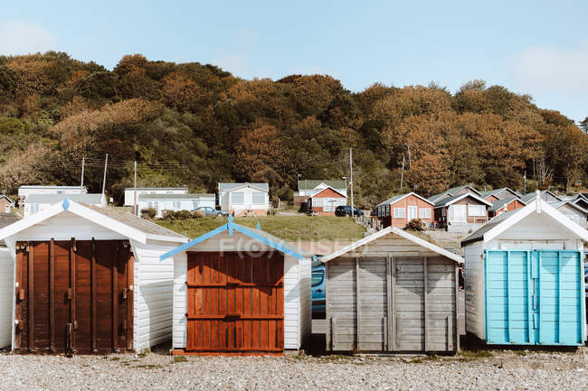 Beach huts of different color with closed doors by woods under blue sky on daytime — Stock Photo