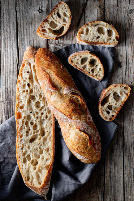 From above whole and sliced appetizing baguettes arranged on napkin against rustic wooden background. — Stock Photo