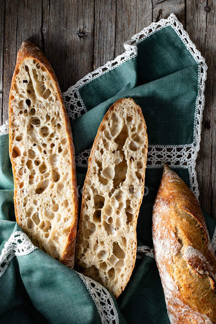 From above whole and halved appetizing baguettes arranged on napkin against rustic wooden background. — Stock Photo