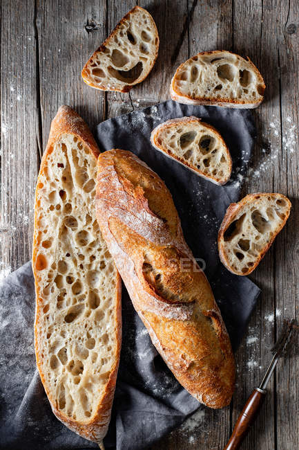 From above whole and sliced appetizing baguettes arranged on napkin against rustic wooden background. — Stock Photo