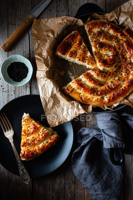 From above of hot baked dish with fresh puff pastry on paper and serving piece of borek on plate. — Stock Photo