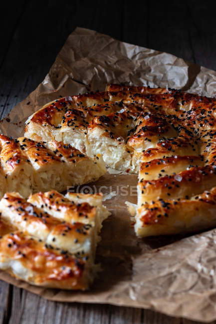 Close-up of hot baked dish with fresh puff pastry and serving piece of borek on paper. — Stock Photo