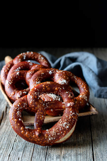 Fresh appetizing pretzels with salt arranged on scoop over old wooden surface — Stock Photo