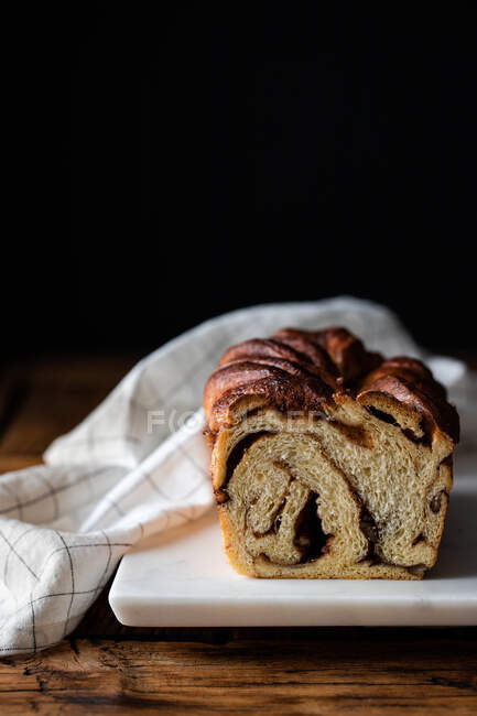 Pan fresco retorcido o babka canela sobre mesa de madera con toalla rayada sobre fondo borroso - foto de stock
