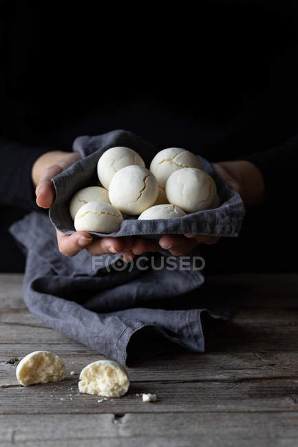 Femme méconnaissable tenant une poignée de délicieux biscuits à la fécule de maïs dans une serviette en tissu sur une table de bois — Photo de stock