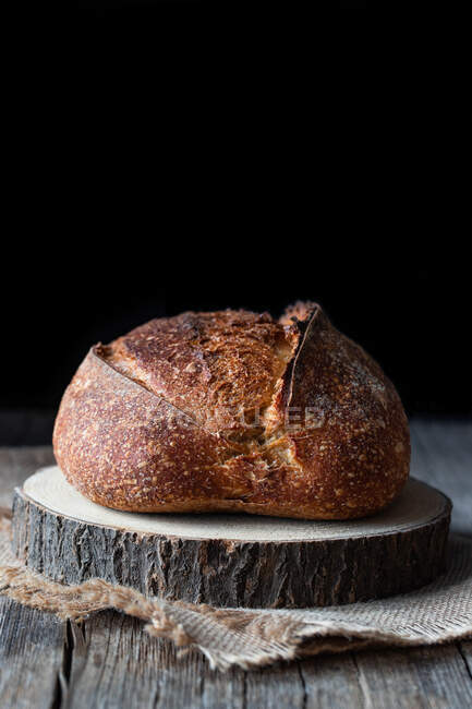 Pão de pão fresco da massa de fonte do país colocado no pedaço de madeira na tabela shabby contra fundo preto — Fotografia de Stock