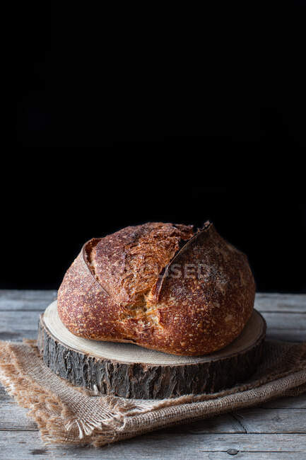 Хліб свіжого сільського кислого хліба, розміщеного на шматочку деревини на обтічному столі на чорному тлі — стокове фото