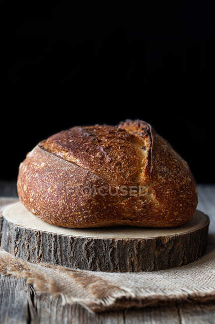 Pane di pasta madre fresca di campagna posto su un pezzo di legno su un tavolo squallido su sfondo nero — Foto stock