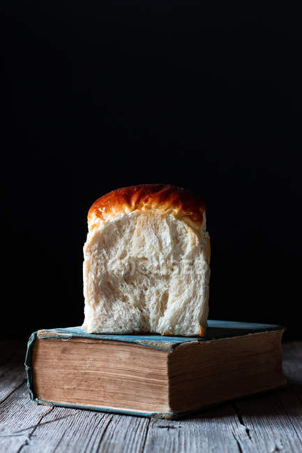 Булочка зі свіжого хліба на старовинній книзі, розміщеній на столі з пиломатеріалів . — стокове фото