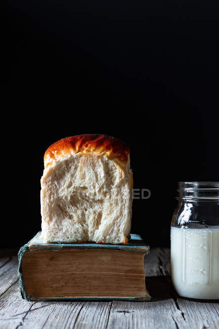 Panino di pane fresco su libro d'epoca e barattolo di latte biologico posto sul tavolo di legname . — Foto stock