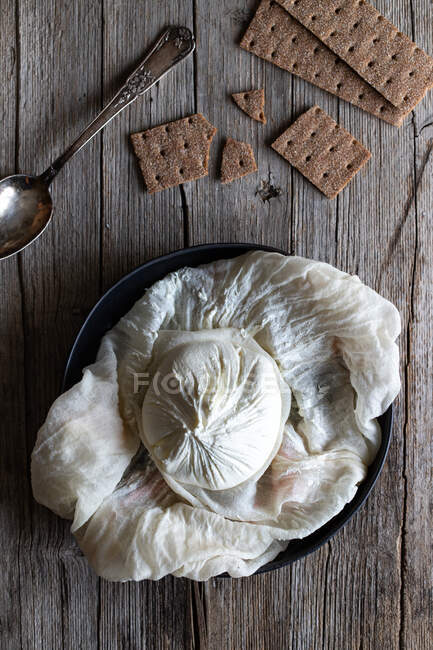 Overhead crunchy crackers and spoon placed near plate with ball of fresh labneh cheese on lumber table — Stock Photo