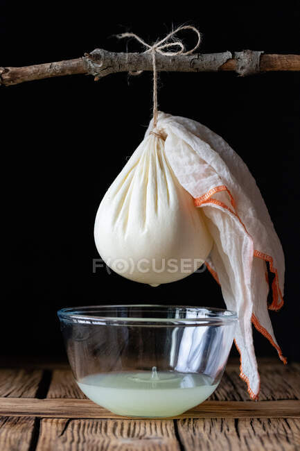 Cloth with ball of fresh labneh cheese hanging on twig over bowl with liquid against black background — Stock Photo