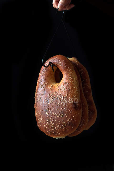 Unrecognizable person holding hook with bunch of fresh Middle Eastern bread against black background — Stock Photo