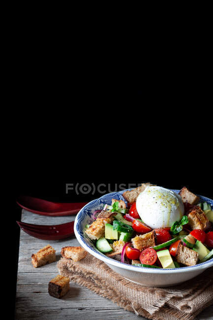 Schüssel mit leckerem Panzanella-Salat auf Tuch auf Holztisch vor schwarzem Hintergrund — Stockfoto