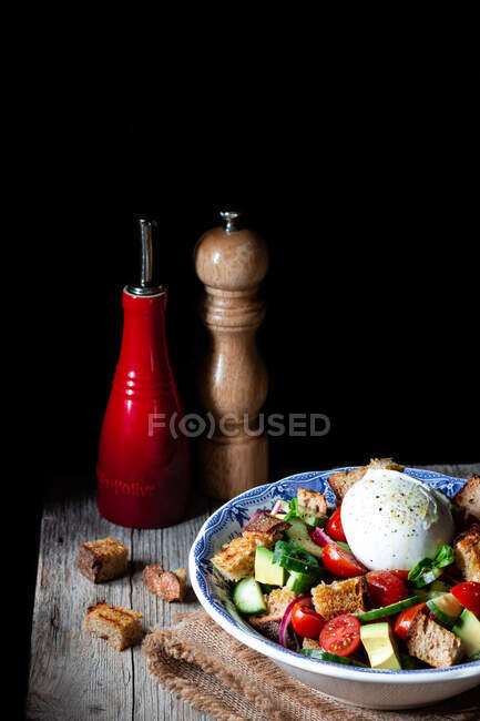 Чаша с вкусным салатом Panzanella помещена на ткань на деревянном столе на черном фоне — стоковое фото