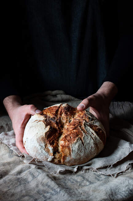 Неузнаваемый человек кладет буханку хлеба на льняную ткань на стол на черном фоне — стоковое фото