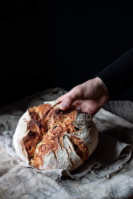 Unbekannter legt Laib Brot auf Leinentuch auf Tisch vor schwarzem Hintergrund — Stockfoto