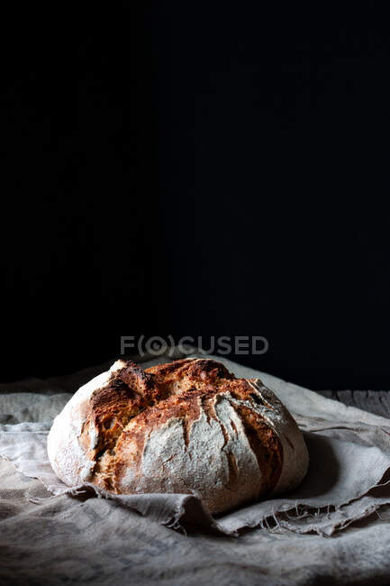 Hoja de pan de masa fermentada fresco país colocado en un pedazo de madera en la mesa de mala calidad sobre fondo negro - foto de stock