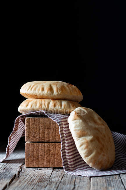 Pão de pita fresco colocado em guardanapo e blocos de madeira na mesa rústica contra fundo preto — Fotografia de Stock