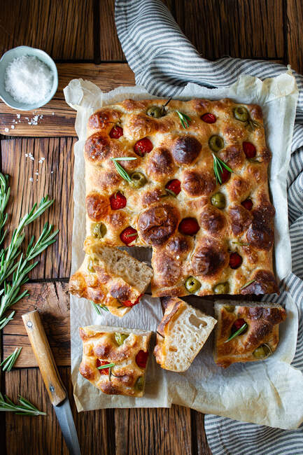 Overhead potato focaccia with fresh rosemary placed near bowl with salt and striped napkin on wooden table — Stock Photo