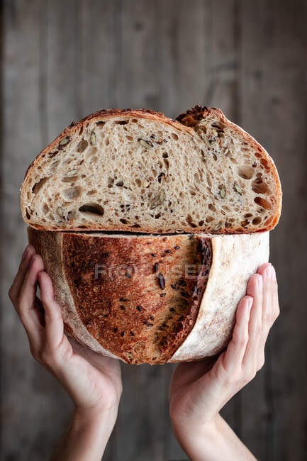 Pessoa irreconhecível mostrando pão fresco meio cortado com sementes contra a parede de madeira — Fotografia de Stock