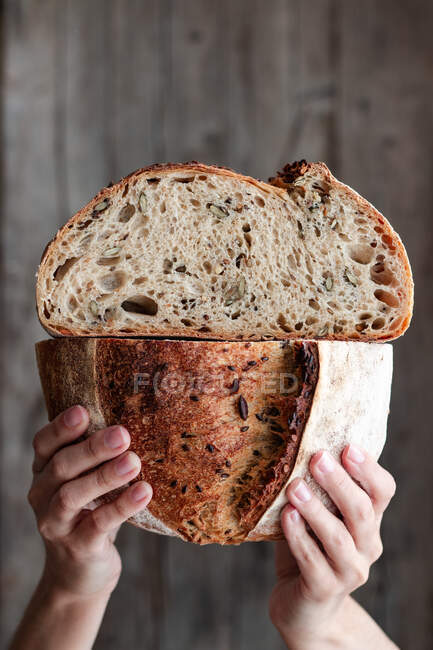 Pessoa irreconhecível mostrando pão fresco meio cortado com sementes contra a parede de madeira — Fotografia de Stock