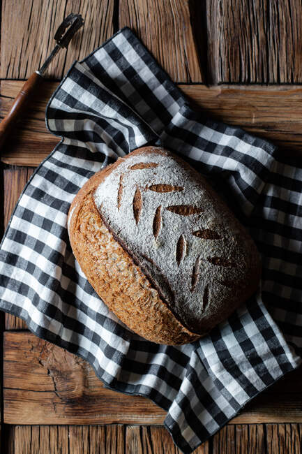 Vue du dessus du pain d'épeautre frais placé sur une serviette à carreaux près de l'outil sur une table à bois — Photo de stock