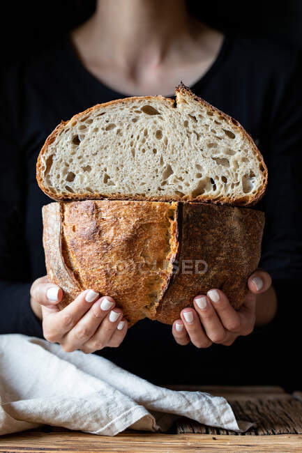 Persona irreconocible mostrando pan fresco a la mitad con semillas contra la pared de madera - foto de stock