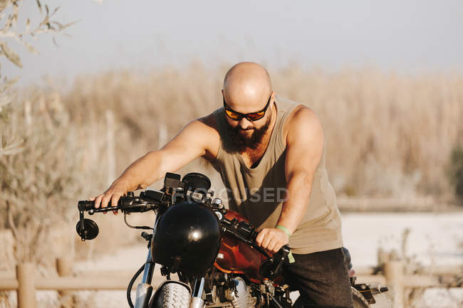 Brutal man sitting on stylish motorcycle in countryside field — Stock Photo