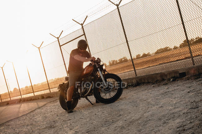 Strong man driving motorcycle at sunset in country — Stock Photo