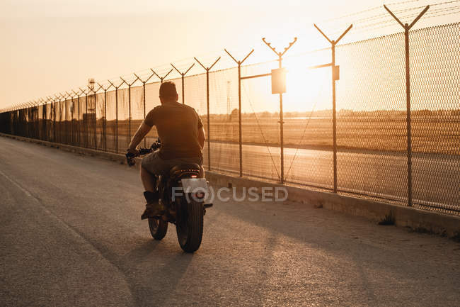 Homem forte dirigindo motocicleta ao pôr do sol, visão traseira — Fotografia de Stock