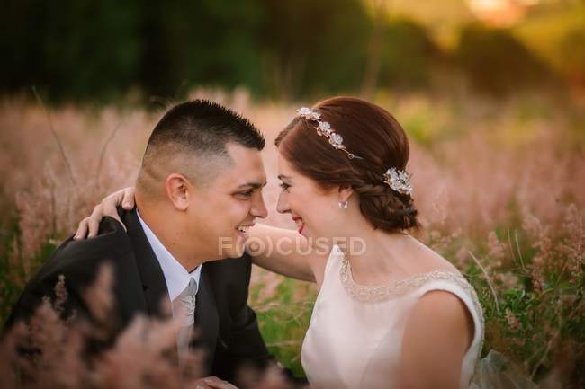 Novia y novio sonrientes abrazándose y besándose en el parque - foto de stock