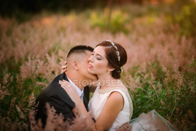 Улыбающиеся жених и невеста обнимаются и целуются в парке — стоковое фото