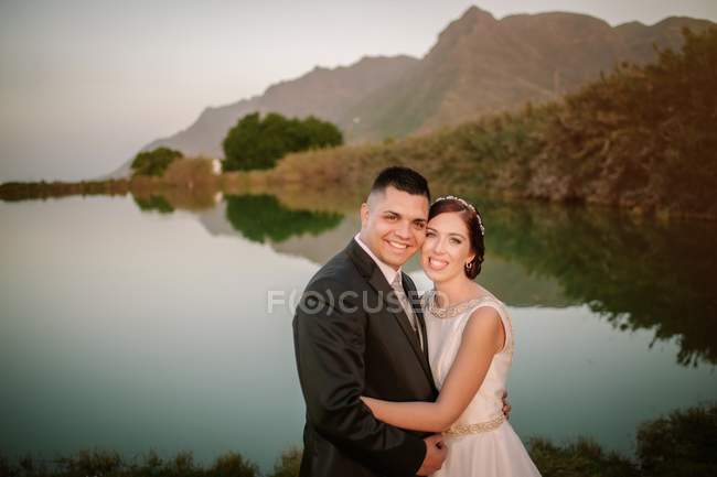 Noiva satisfeita e noivo no fundo do lago cercado por montanhas — Fotografia de Stock