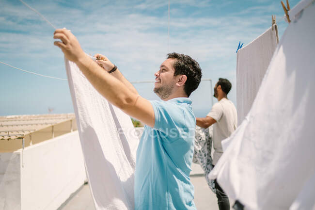 Hommes multiraciaux accrochant des vêtements dans le jour lumineux — Photo de stock