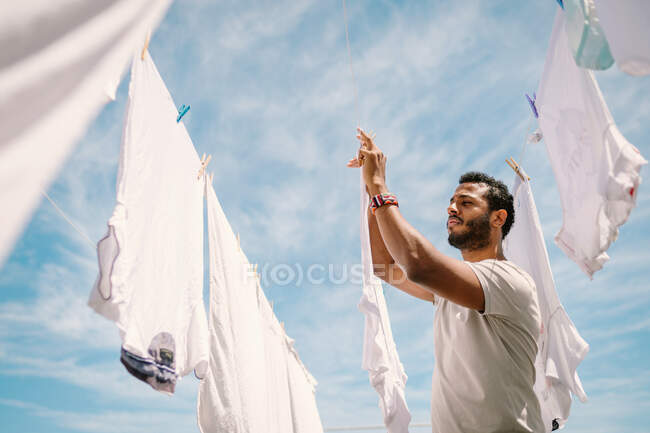 Diligent ethnic man hanging t-shirt on rope — Stock Photo