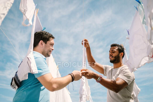 Vielrassige Männer hängen Kleider bei hellem Tag auf — Stockfoto